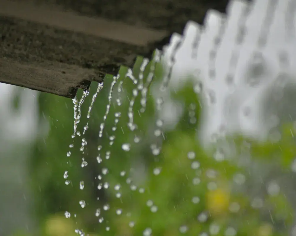 Rainwater overflowing from a blocked gutter on a UK house during heavy rain